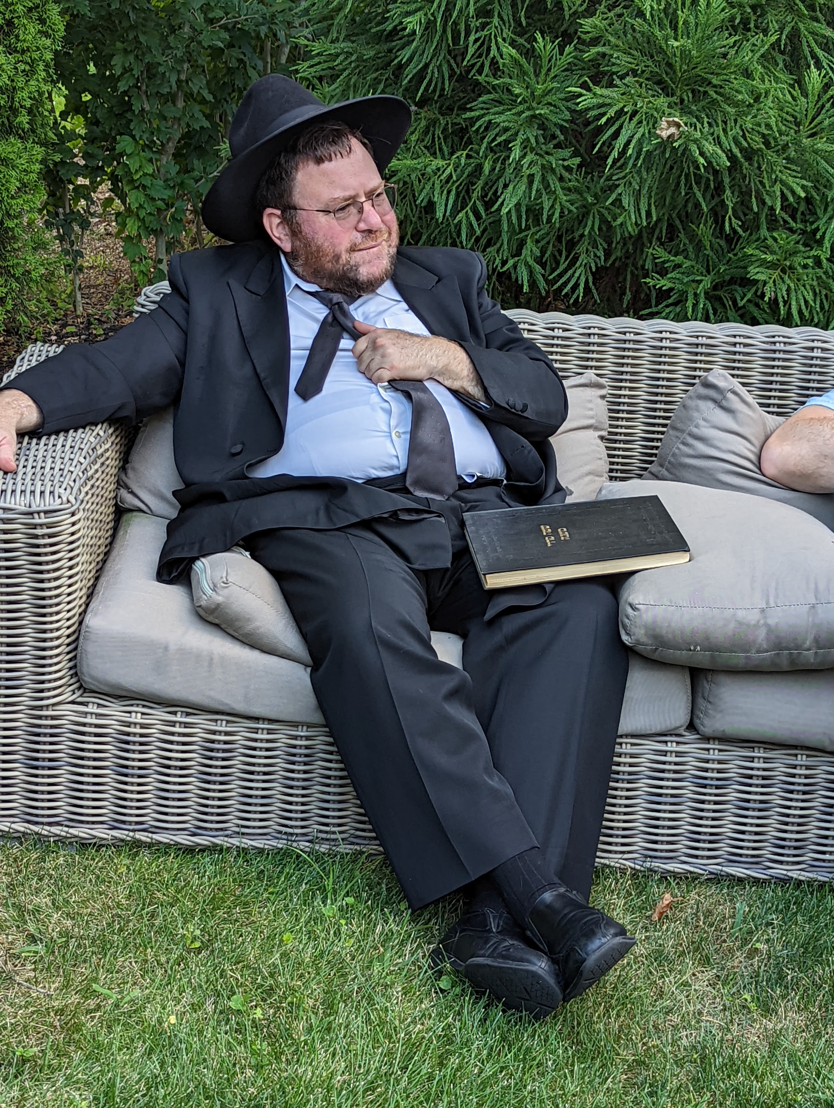 Rabbi Bechhofer relaxing on the garden sofa with a sefer at the 2022 Arizal Dinner